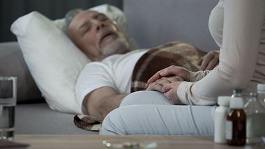 Mann schläft während Frau seine Hand hält - Foto: iStock/Motortion