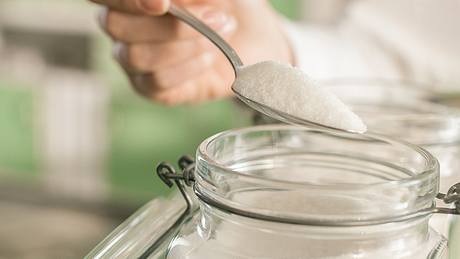 Frau nimmt einen Esslöffel Zucker aus einem Behälter. - Foto: iStock/hoozone