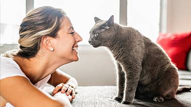 Eine Frau sitzt vor ihrer Katze und lächelt sie an - Foto: istock_LSOphoto
