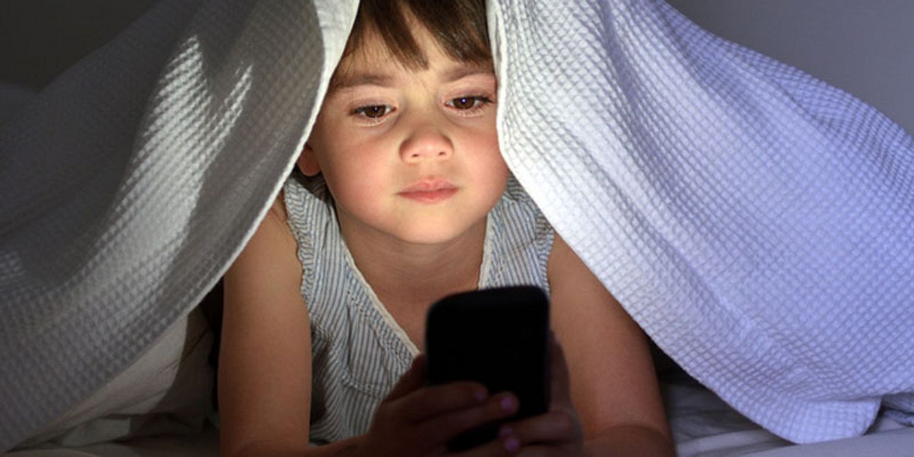 Ein Kind schaut unter der Decke auf sein Smartphone