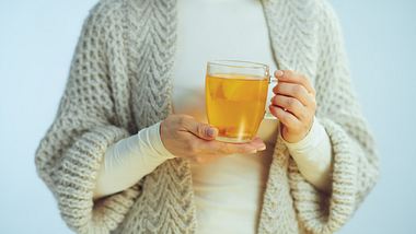 Man sieht einen Frauenoberkörper, die Frau trägt Pulli und Strickjacke und hält ein Teeglas in den Händen - Foto: iStock-1203134730 CentralITAlliance