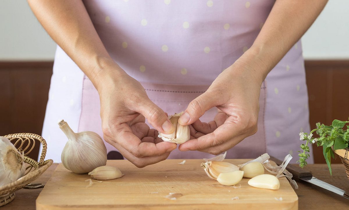 Frau schneidet Knoblauch auf einem Holzbrett