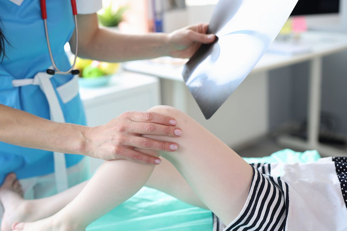 Ärztin mit Röntgenbild legt Kind die Hand aufs Knie