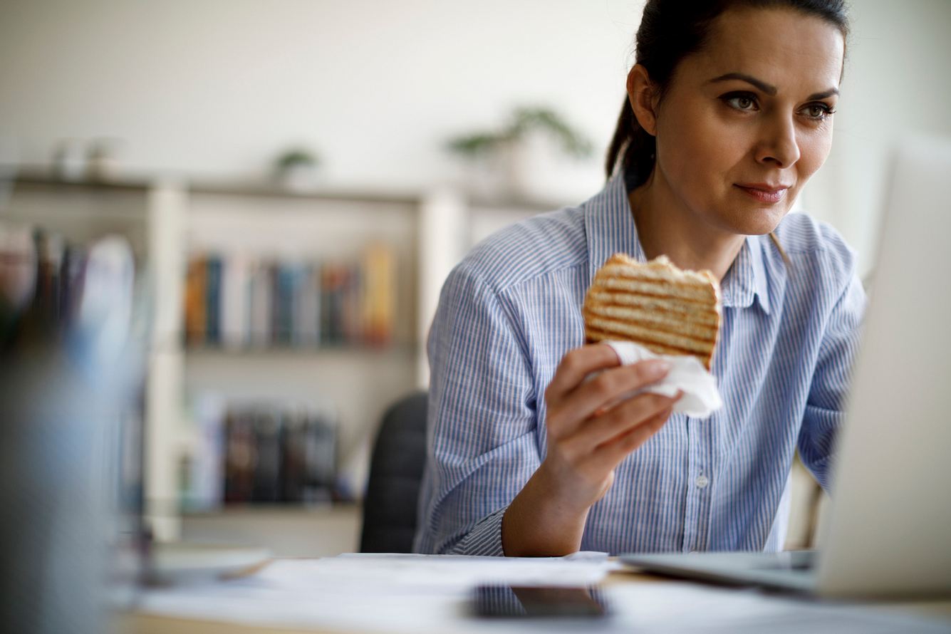 Eine Frau isst Brot, während sie am Laptop arbeitet