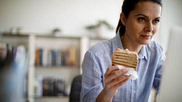 Eine Frau isst Brot, während sie am Laptop arbeitet - Foto: iStock_damircudic