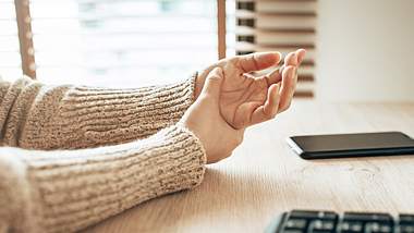 Eine Frau sitzt am Schreibtisch und massiert ihre Hände - Foto: istock_interstid