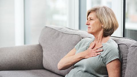 Eine Frau sitzt auf dem Sofa und hält sich die Brust - Foto: iStock/PeopleImages