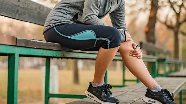 Eine Joggerin sitzt auf einer Bank und hält sich das Knie - Foto: iStock/PixelsEffect