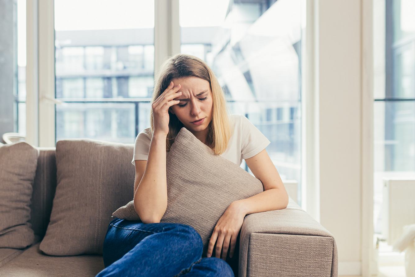 larvierte-depression Eine Frau sitzt mit Kopfschmerzen auf einem Sofa