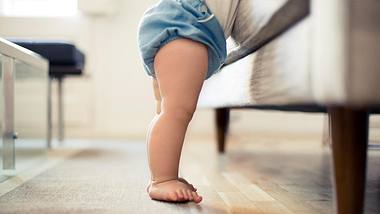 Ein Baby steht vor einem Sofa - Foto: istock_OrbonAlija