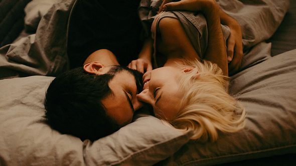 Ein Paar küsst sich im Bett - Foto: iStock/AleksandarNakic