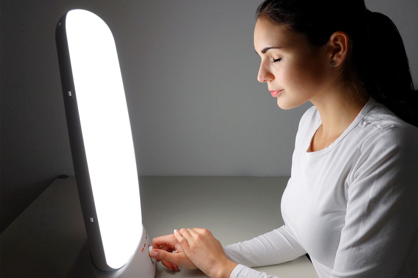 Frau sitzt vor einer Lampe zur Lichttherapie