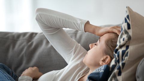 Eine Frau liegt mit Long Covid erschöpft auf dem Sofa - Foto: istock/fizkes