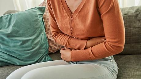 Frau fasst sich an schmerzenden Bauch - Foto: iStock / LaylaBird