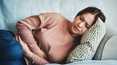 Eine Frau liegt mit Magenschmerzen auf dem Sofa - Foto: iStock_PeopleImages