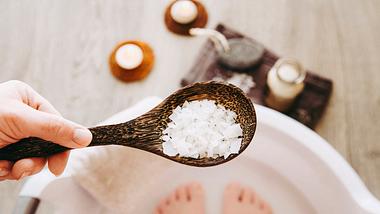 Frauenfüße in einer Wanne mit Wasser; ein Holzlöffel mit Salzflocken - Foto:  iStock/Helin Loik-Tomson