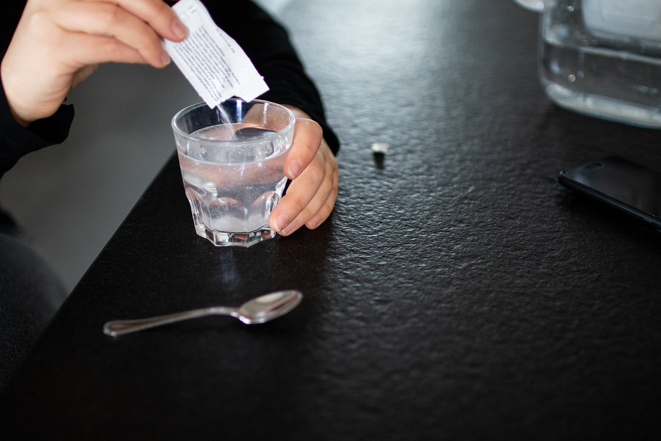 Eine Frau rührt Trinkgranulat mit Magnesium in ein Glas Wasser