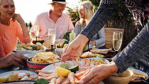 Gruppe sitzt am Tisch und genießt ein gemeinsames Essen - Foto: SolStock/iStock