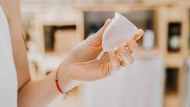 Eine Frau hält eine Menstruationstasse in der Hand - Foto: istock_NataliaDeriabina