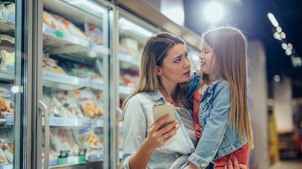Eine Frau kauft mit einem Kind auf dem Arm ein - Foto: iStock/bernardbodo 