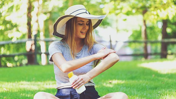 Eine Frau sitzt auf einer Wiese und cremt sich mit Sonnencreme ein - Foto: iStock/Melpomenem