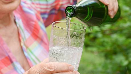 Eine Frau gießt Mineralwasser in ein Glas - Foto: IMAGO/Petra Schneider