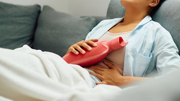 Frau mit Wärmflasche auf dem Sofa - Foto: iStock/Drazen Zigic