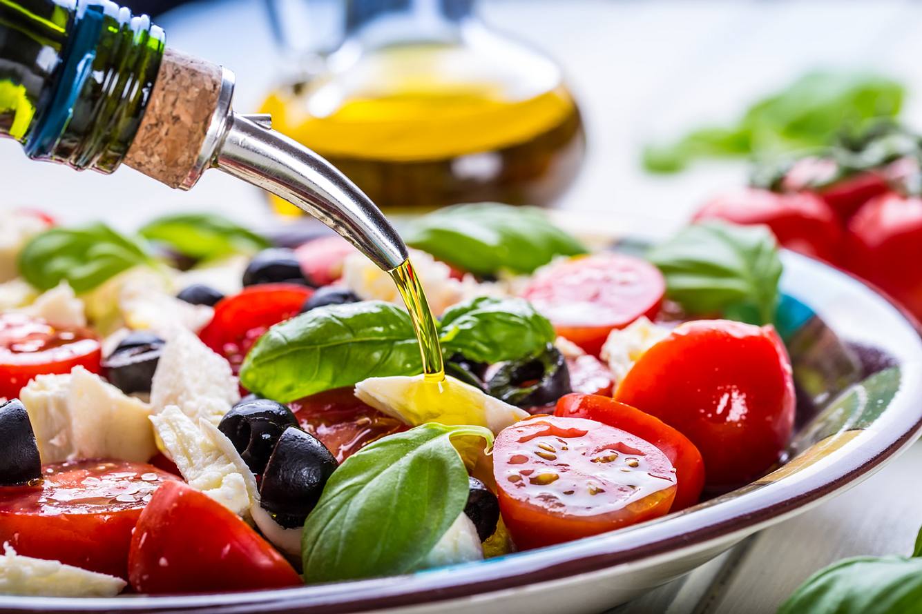 Mediterraner Salat auf einem Teller, Olivenöl wird darübergegeben