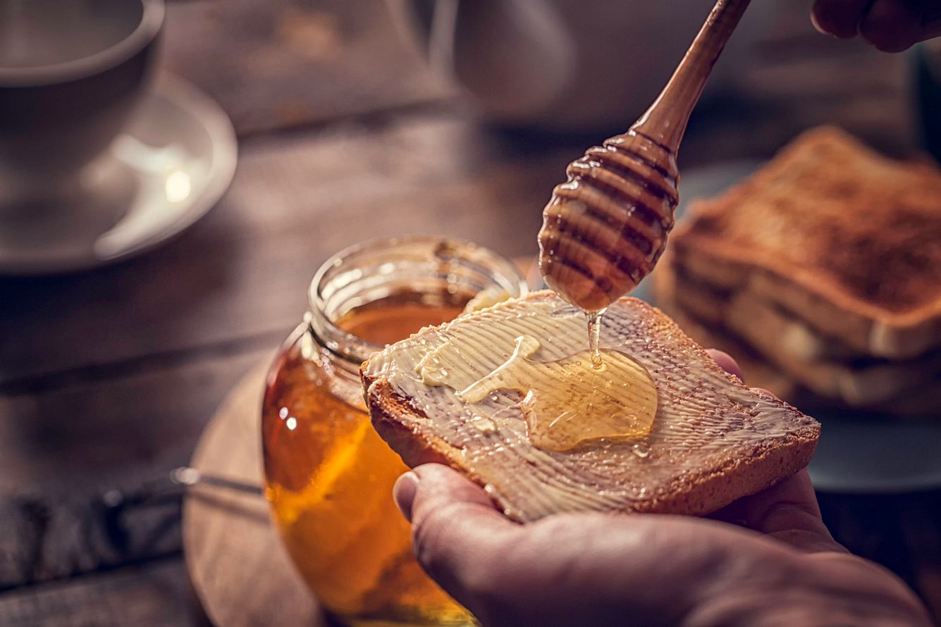 Hand hält Brot mit Butter und träufelt Honig darauf