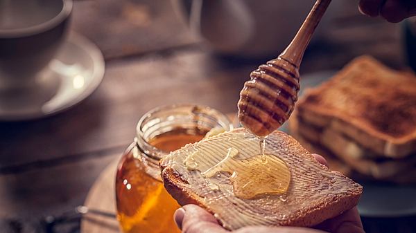 Hand hält Brot mit Butter und träufelt Honig darauf - Foto: iStock/GMVozd