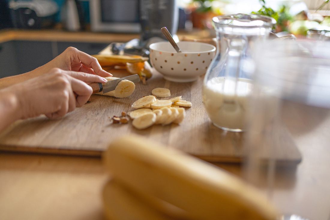 muedigkeit-nach-fruehstueck- Hand schneidet eine Banane, im Vordergrund ganze Bananen