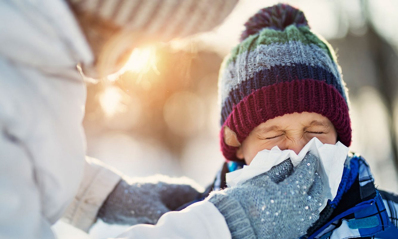 Mutter putzt ihrem Kind draußen im Winter die Nase
