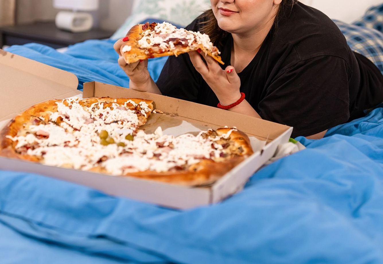 Frau isst Pizza im Bett
