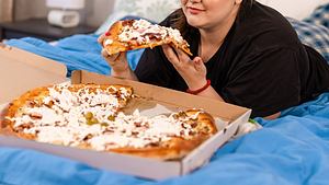 Frau isst Pizza im Bett - Foto: iStock/RealPeopleGroup