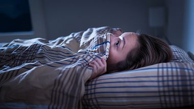 Eine Frau liegt mit weit aufgerissenen Augen im Bett - Foto: iStock_Tero Vesalainen