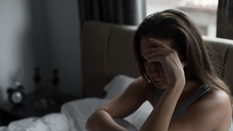 Frau sitzt im Bett und hält sich den Kopf. - Foto: iStock/bymuratdeniz