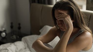 Eine Frau sitzt nachts wach in ihrem Bett - Foto: iStock/bymuratdeniz