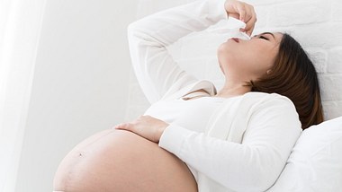 Schwangere Frau sitzt mit Nasenbluten auf dem Sofa - Foto: iStock/comzeal
