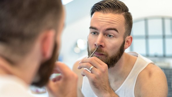 Mann steht vorm Spiegel und schneidet sich die Nasenhaare - Foto: iStock/LarsZahnerPhotography