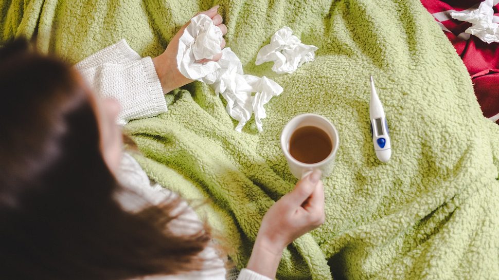 erkältete Frau sitzt mit Taschentüchern und Tee auf der Couch - Foto: istock sestovic