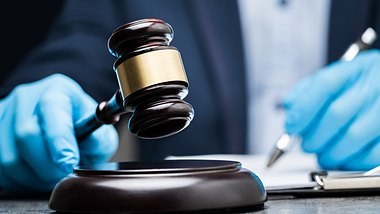 Ein Richter in Handschuhen notiert sich etwas mit Richterhammer in der Hand - Foto: istock_AndreyPopov