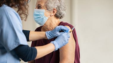 Ältere Frau mit medizinischer Maske wird von jüngerer Ärztin in Schutzkleidung geimpft - Foto: istock/﻿Ridofranz