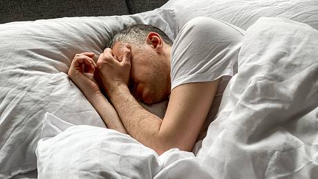 Mann schläft und hält sich Hände vor das Gesicht - Foto: iStock/Alla Tsyganova 