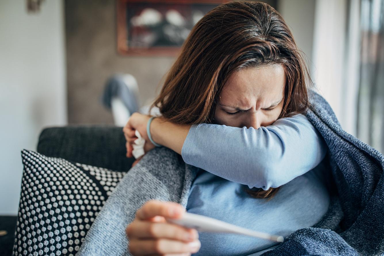 Eine Frau liegt auf dem Sofa und hustet in die Armbeuge Eine Frau liegt auf dem Sofa und hustet in die Armbeuge