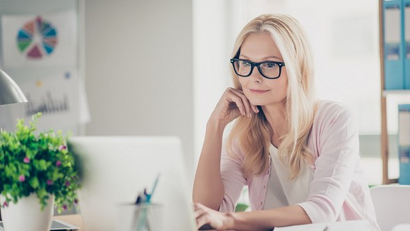 blonde Frau sitzt mit Brille am Laptop - Foto: iStock/Deagreez