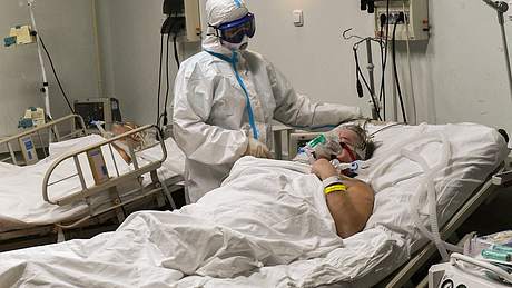 Mann im Krankenbett auf Intensivstation, daneben Arzt in Vollschutz - Foto: IMAGO / SNA