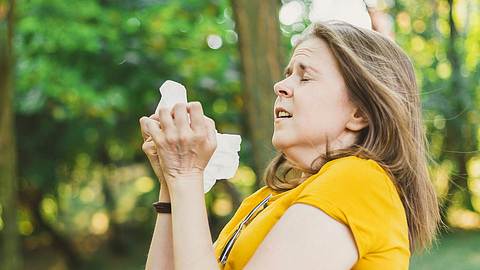 Frau mit zusammengekniffenen Augen und Taschentuch muss niesen - Foto: istock 1180014622 Madrolly