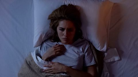 Eine Frau liegt verängstigt in ihrem Bett - Foto: iStock / Motortion