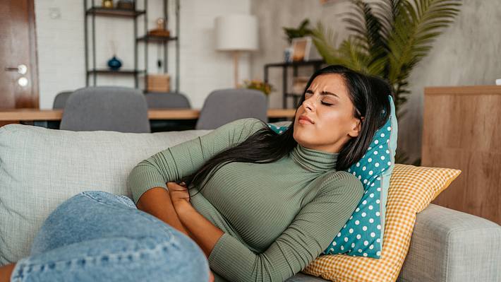 Eine Frau liegt mit Bauchschmerzen auf einem Sofa - Foto: iStock_urbazon
