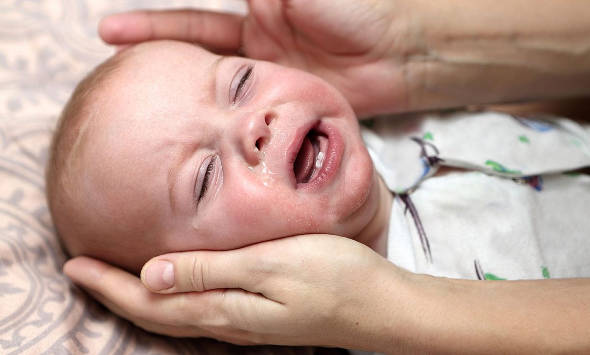 Ein Baby weint und seine Mutter hält ihre Hände an seine Ohren